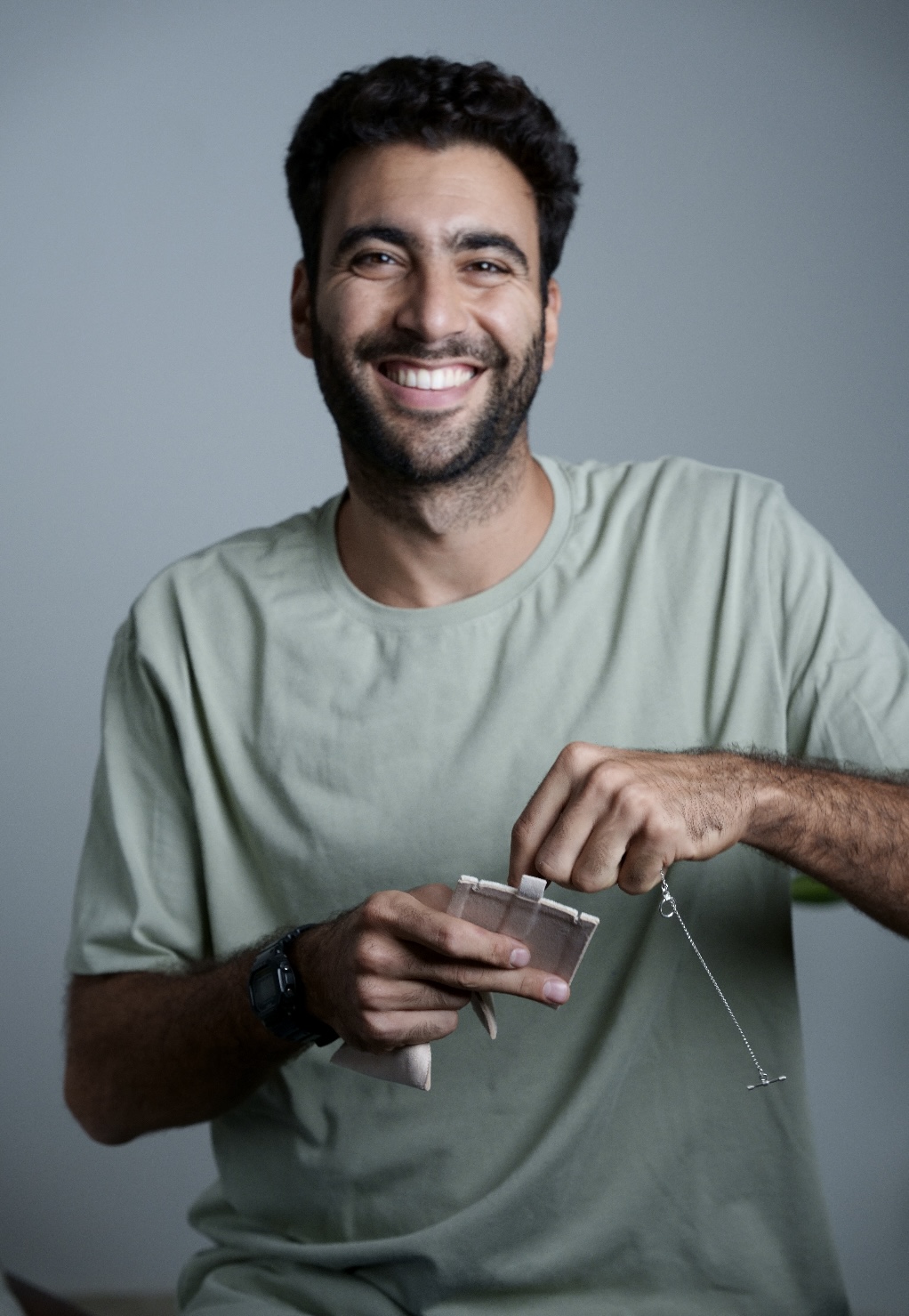 Robeir Barsoum, a smiling jewelry maker, holding a delicate silver necklace in his workshop